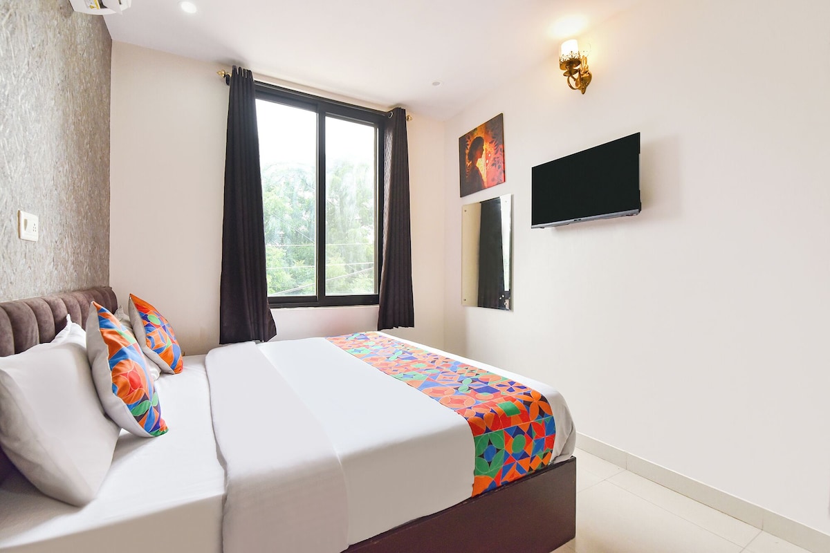 Une chambre d’hôtel avec un lit, un téléviseur à écran plat, une fenêtre avec des rideaux et un tableau au mur.