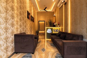 A hotel reception area with a reception desk, two sofas, patterned wallpaper, and a ceiling fan. - Fabhotel Prime Stay Inn (Jaipur)