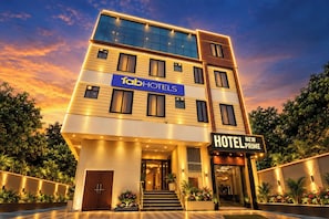 Un hôtel à plusieurs étages, reconnaissable à son enseigne bien visible « Tab Hotels », à l’enseigne « Hotel New Prime » et à son entrée bien éclairée, agrémentée d’un escalier.