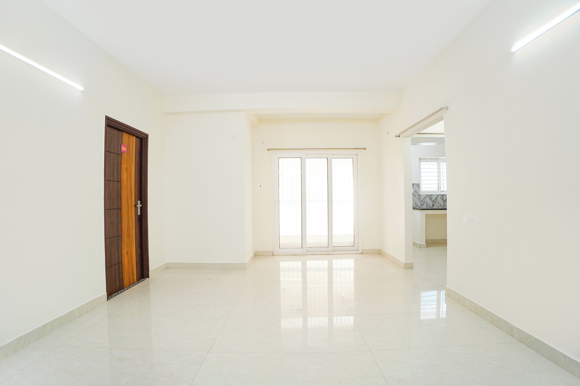 A spacious, well-lit hallway with a wooden door and a sliding glass door leading to a balcony.