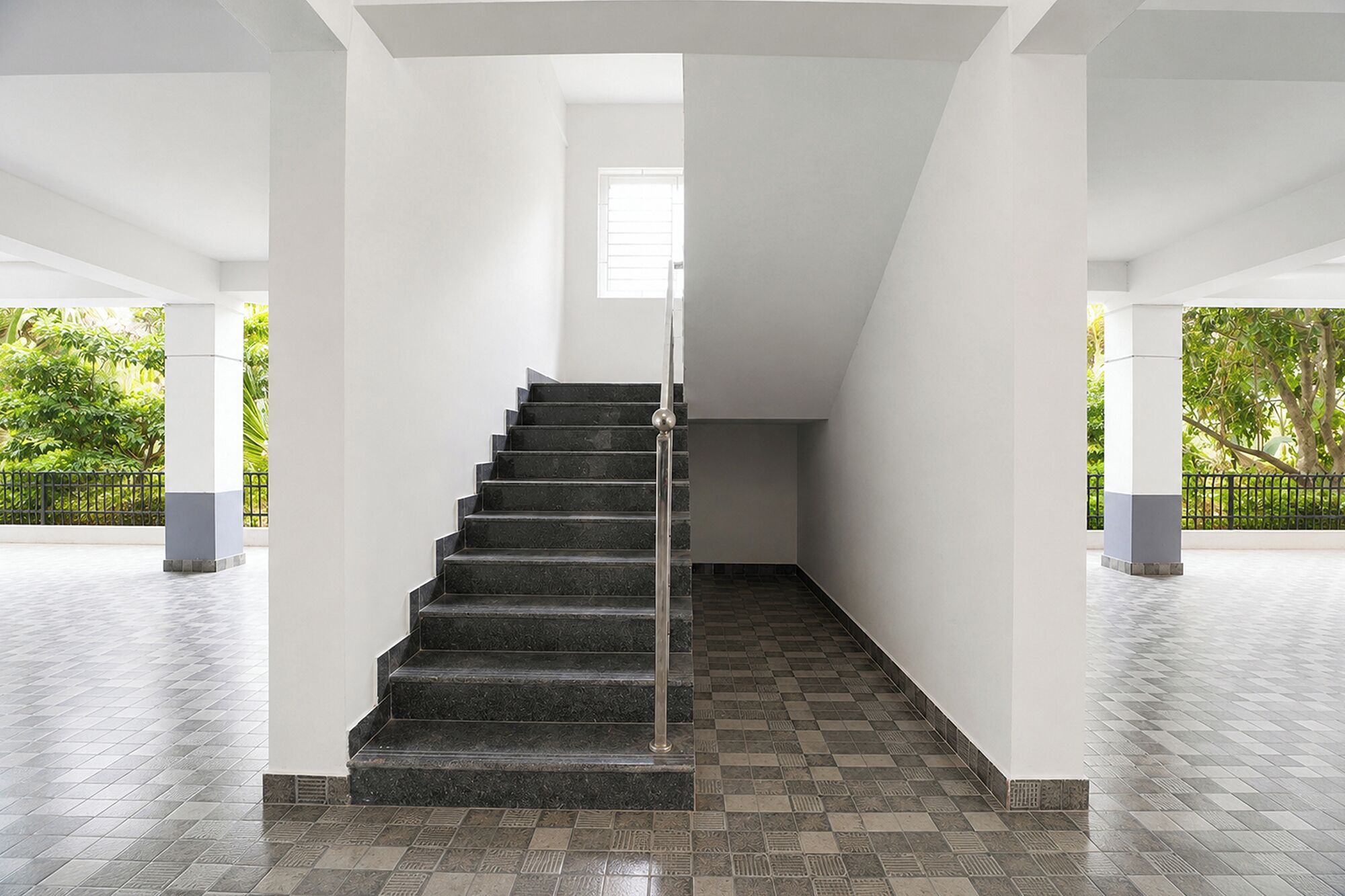 Una escalera con barandilla de metal, paredes blancas y baldosas de suelo con diseño.