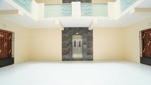 Un hall espacioso con piso de mármol, un ascensor central y una escalera con barandilla de color claro.