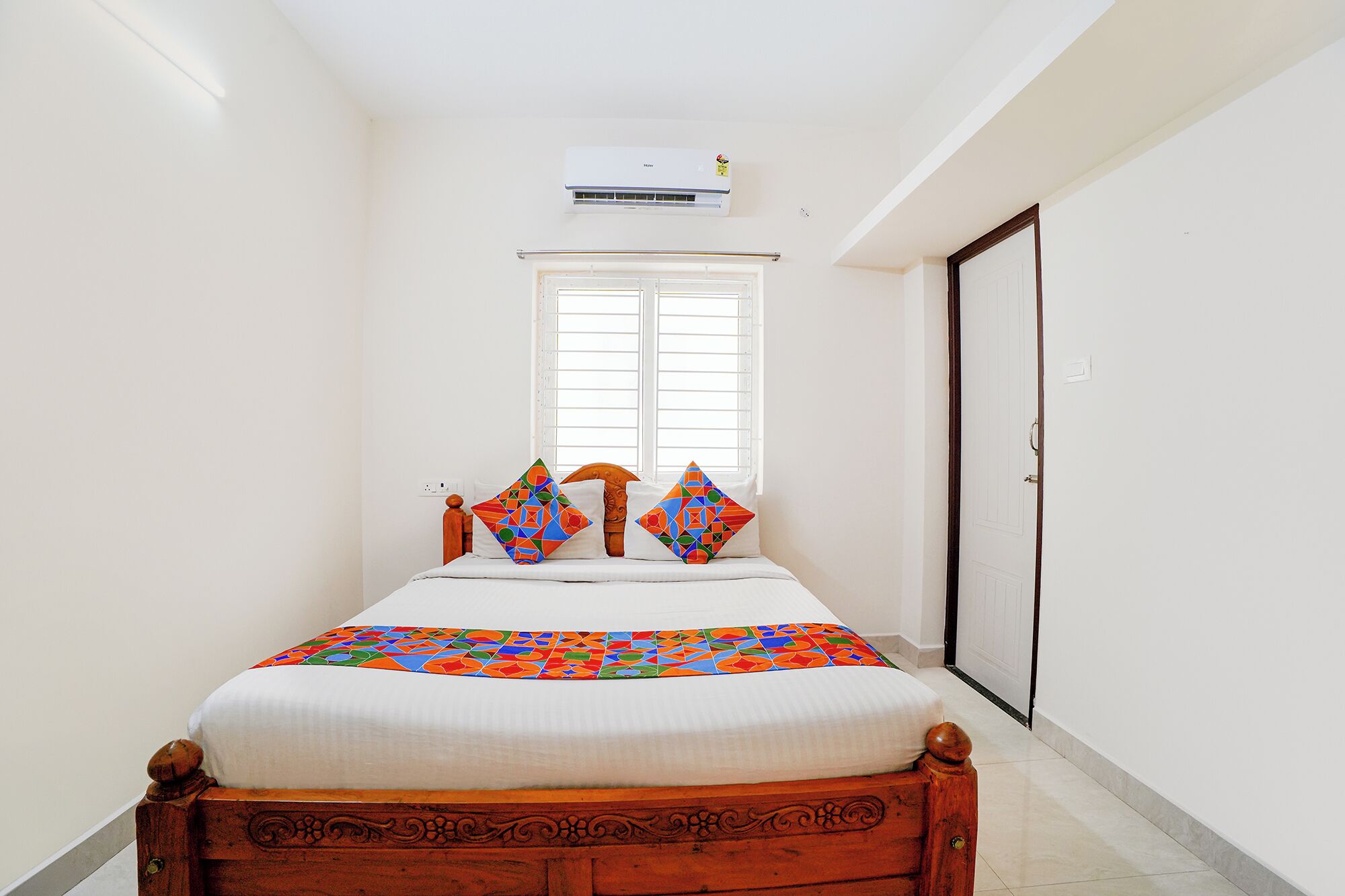 A bedroom with a bed, a window, an air conditioning unit, and a door.