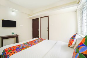 Una habitación de hotel con una cama, un escritorio, un televisor y una puerta.