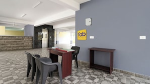 Un hall de hotel con mostrador de recepción, sillas, un letrero en la pared que dice 'fab hotels' y piso de baldosas.