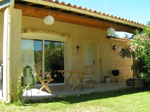 Eine überdachte Terrasse mit Tisch, Stühlen, einer Tür und Kübelpflanzen.