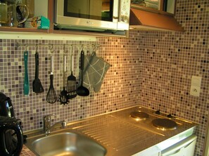 A kitchen with a stainless steel sink, a microwave, and various utensils hanging on the wall. - Little butterfly (Carpentras)