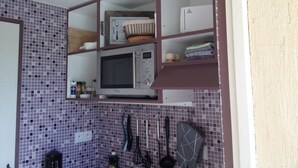 A kitchen with a microwave, shelves, and tiled backsplash. - Little butterfly (Carpentras)