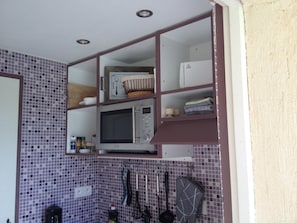 Eine Küche mit Mikrowelle, Regalen und einer gefliesten Rückwand.
