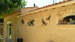 A building exterior with a tiled roof, a wooden chair, a grill, and potted plants. - Little butterfly (Carpentras)
