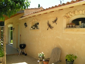 A building exterior with a tiled roof, a wooden chair, a grill, and potted plants.