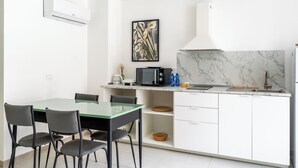 Moderni keittiö, jossa on valkoiset kaapit, marmoripintainen välitila ja ruokailutila, jossa on lasipöytä ja -tuolit.