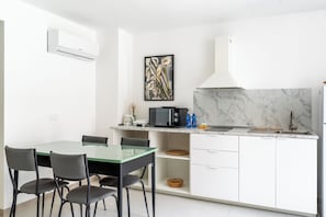 A modern kitchen with white cabinets, a marble backsplash, and a dining area with a glass table and chairs. - Dinologo Modern Flat by Wonderful Italy (Siracusa)