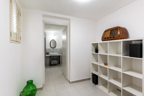A hallway with a white tiled floor, a green vase, a radio on a shelf, and a door leading to a bathroom. - Dinologo Modern Flat by Wonderful Italy (Siracusa)