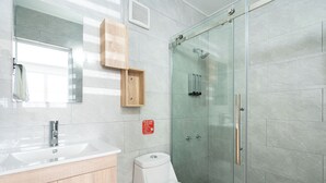 Un baño moderno con cabina de ducha de vidrio, inodoro blanco, lavamanos con gabinete de madera y espejo.