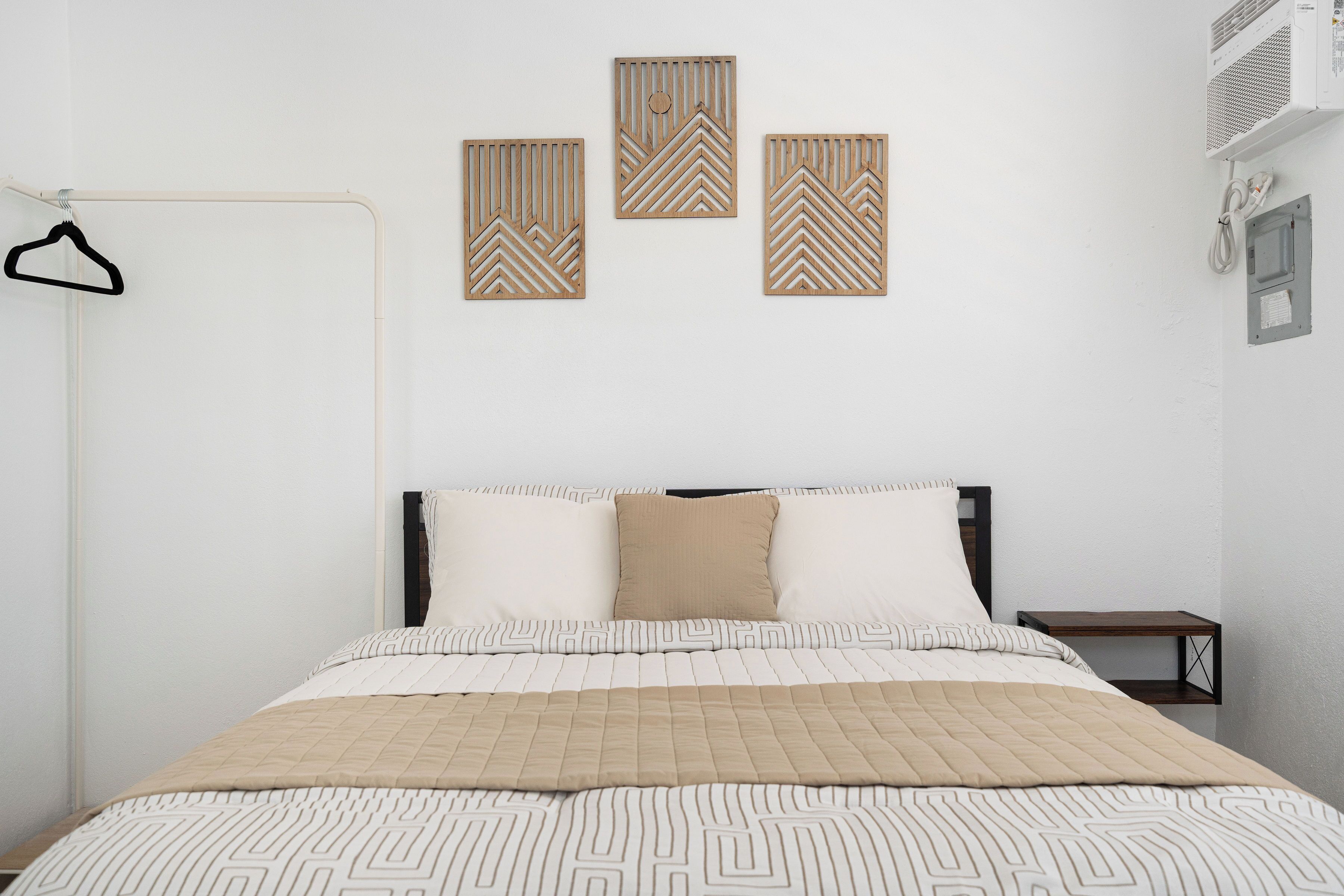 Un dormitorio con una cama, perchero y tres paneles decorativos en la pared.