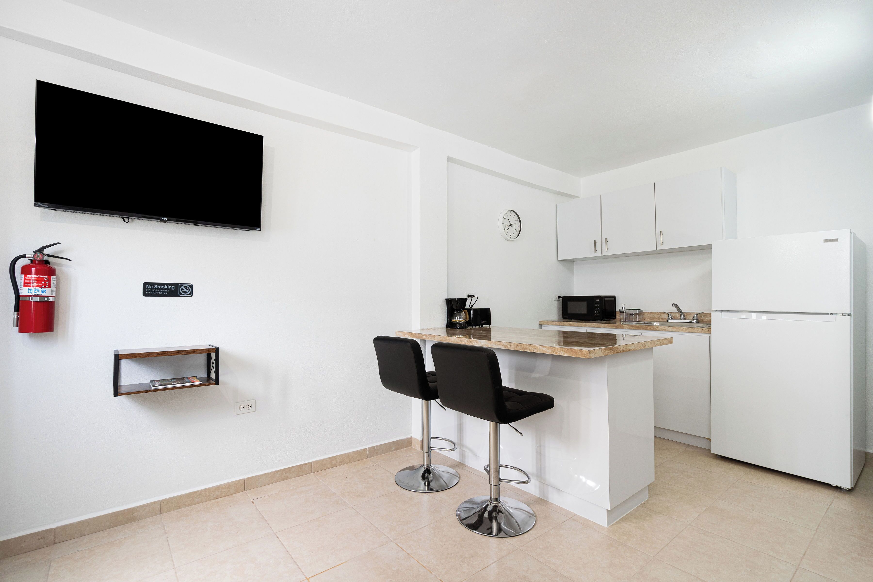 Una cocina moderna con televisión de pantalla plana, un reloj y un refrigerador.