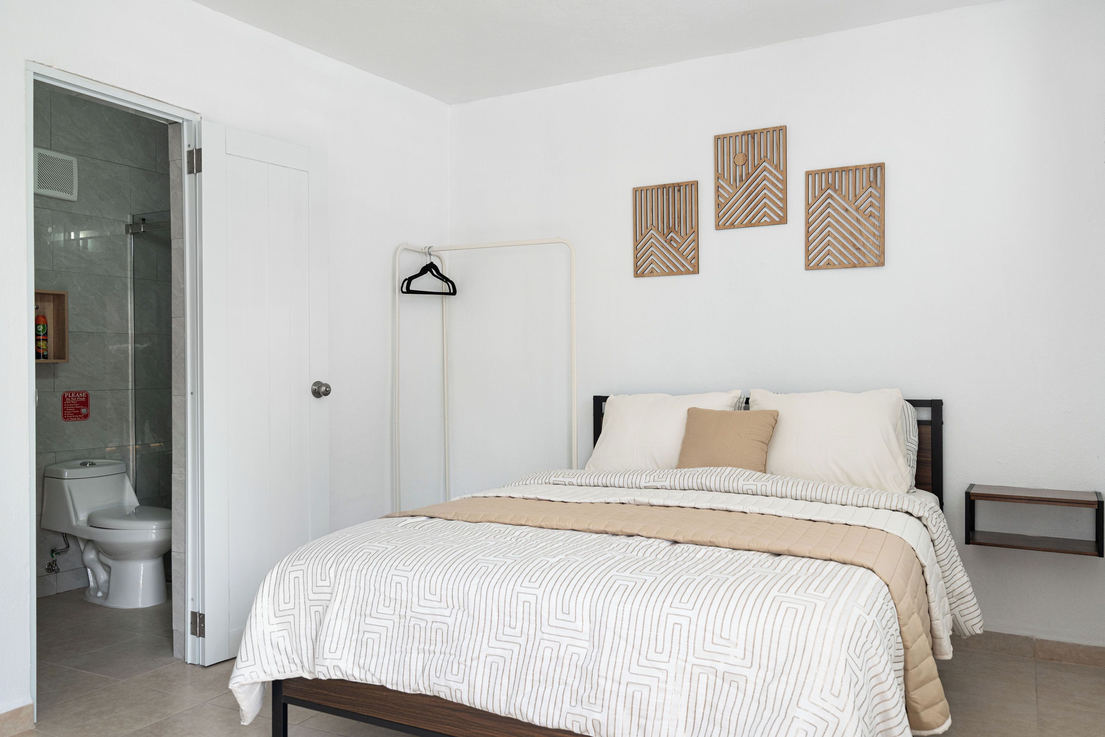 A bedroom with a bed, a bedside table, a hanging coat rack, and a shower area.