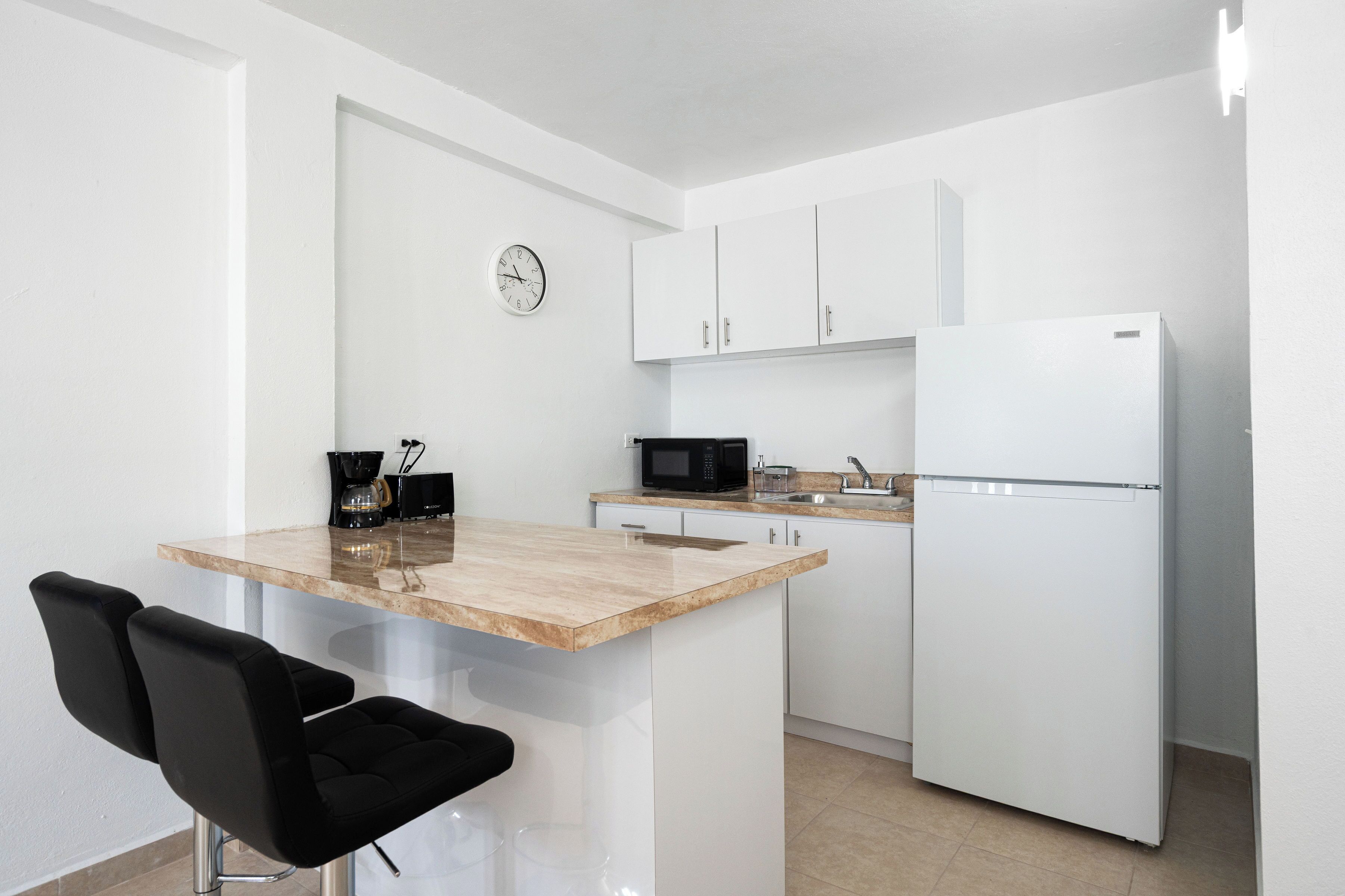 Una cocina compacta con una isla central, microondas, refrigerador y cafetera.