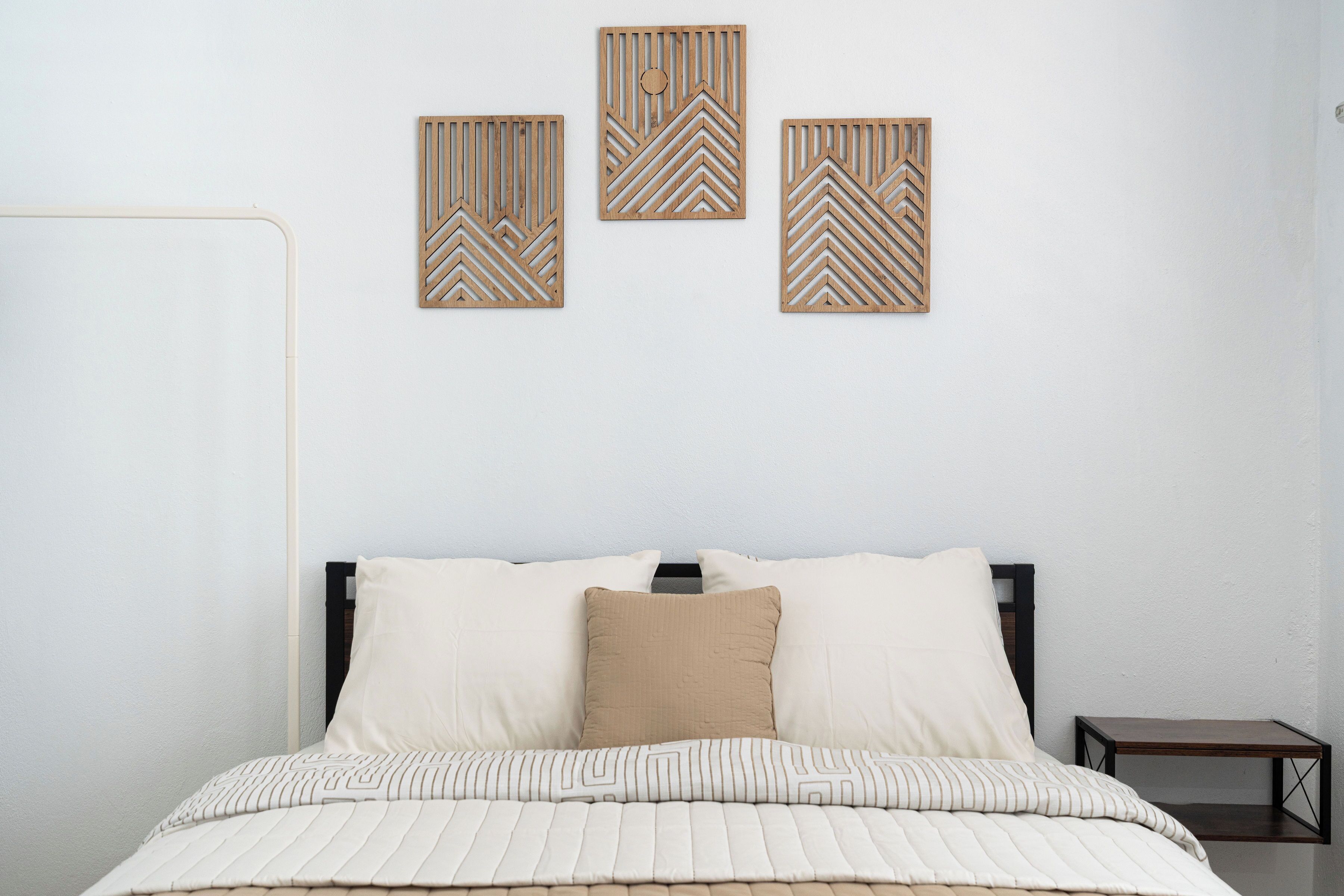 Un dormitorio con cama, almohadas, una mesita de noche y tres paneles decorativos en la pared.