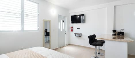 Habitación de hotel moderna con cama, televisión, pequeño bar y baño.
