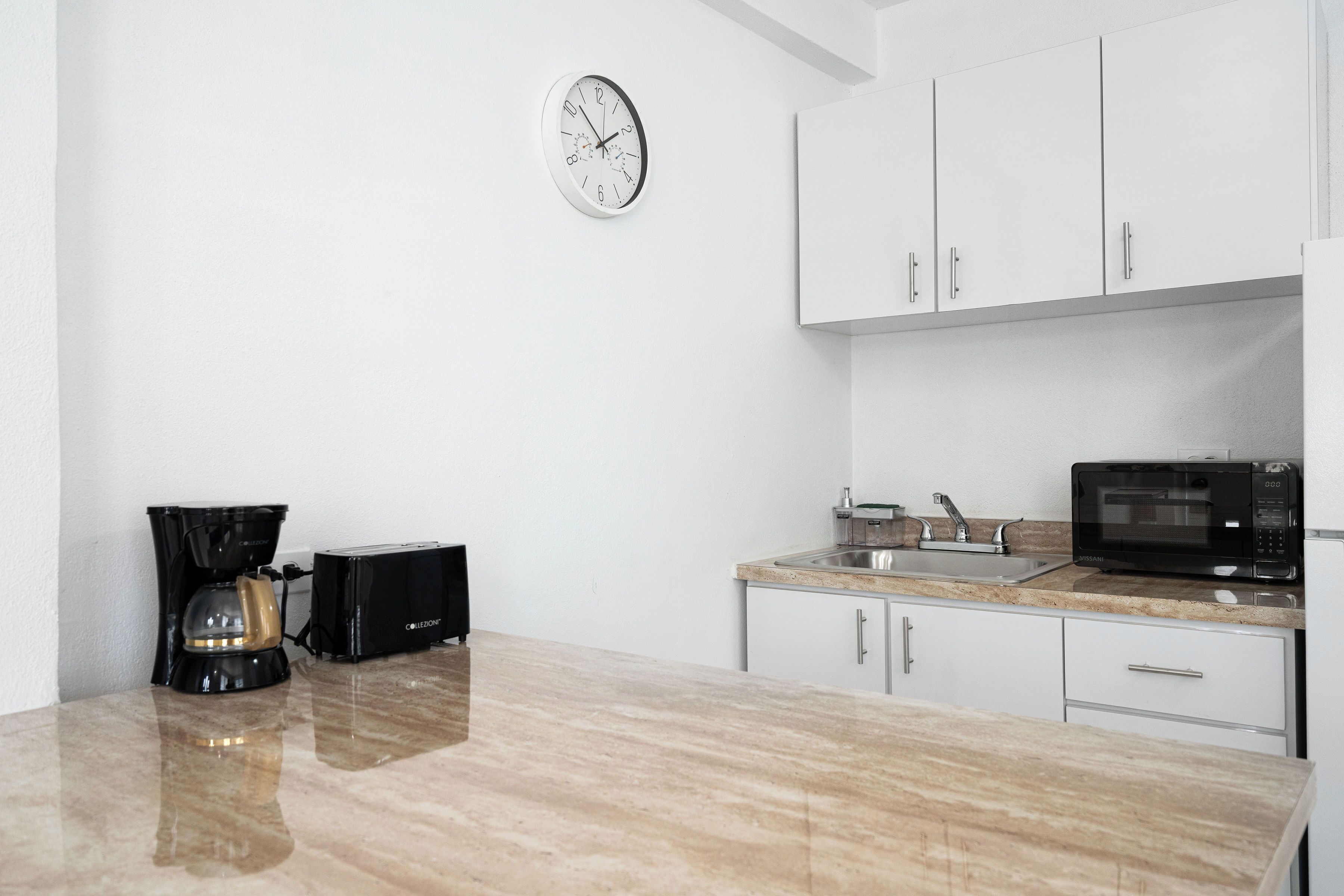 A kitchen with white cabinets, a stainless steel sink, a coffee maker, a toaster, and a microwave.