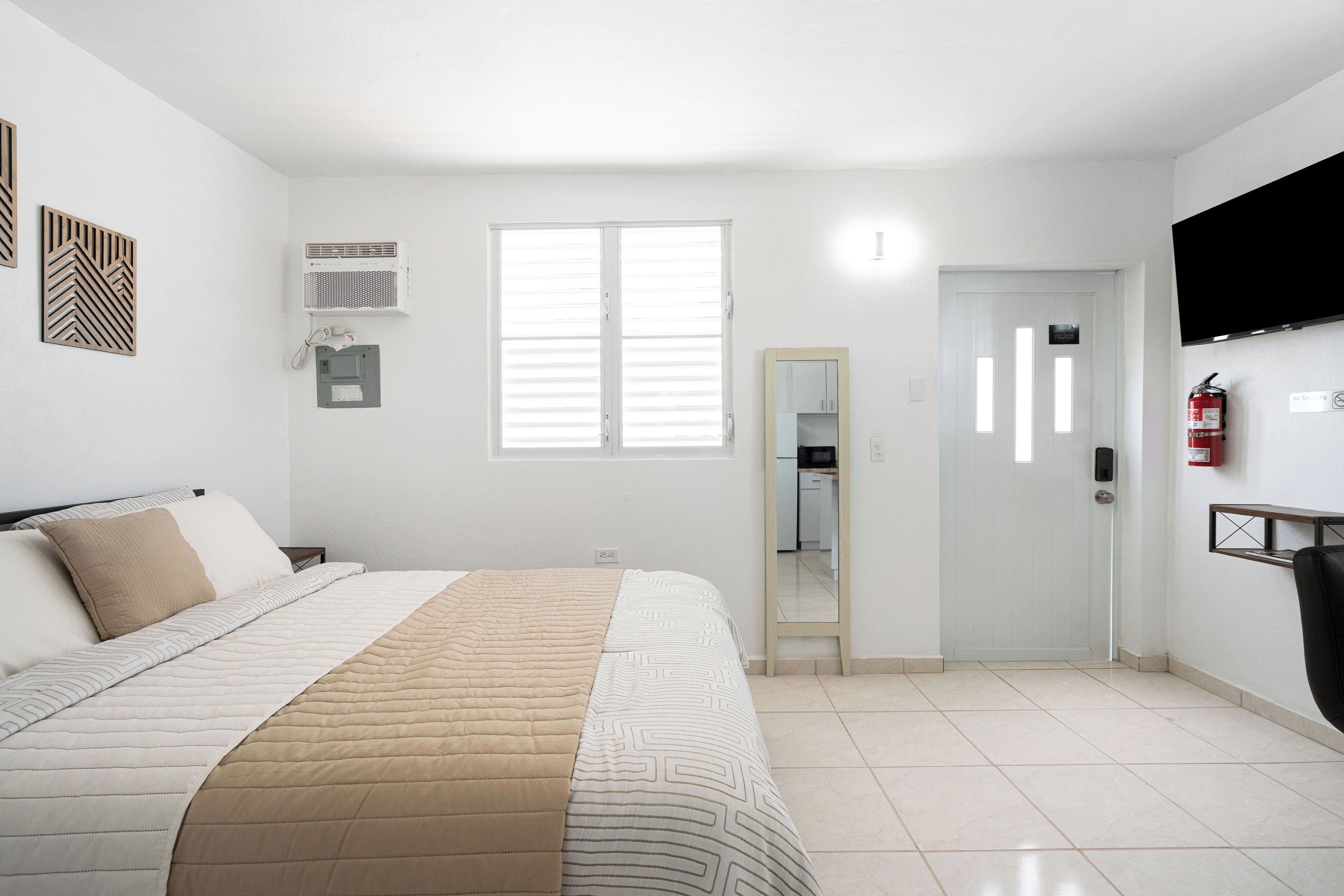 A bedroom with a bed, a window, a door, and a wall-mounted air conditioner.
