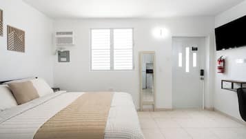 A bedroom with a bed, a window, a door, and a wall-mounted air conditioner.