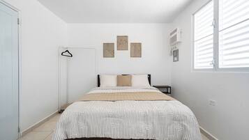Ein Schlafzimmer mit einem Bett, einem Kleiderhaken und einem Fenster mit Jalousien.