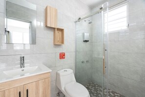Un baño moderno con cabina de ducha de vidrio, inodoro blanco y un mueble de madera sobre el lavabo.