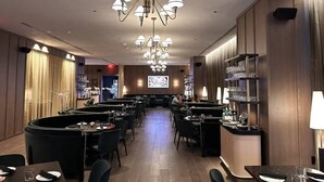 Um restaurante com várias mesas e cadeiras, um espaço de bar e uma tela grande exibindo conteúdo.
