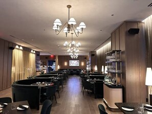 Ein Restaurant mit mehreren Tischen, Stühlen, einer Bar und einem großen Bildschirm, der Inhalte zeigt.