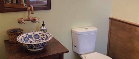 A bathroom with a wooden vanity, a blue and white ceramic basin, a white toilet, and a wooden shelf with various items.