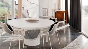 A modern dining area with a round table and chairs, a staircase, and a kitchen in the background. - Casas Bioclimáticas Iter El Dispositivo (Granadilla de Abona)