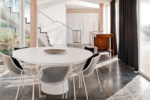 A modern dining area with a round table and chairs, a staircase, and a kitchen in the background. - Casas Bioclimáticas Iter El Dispositivo (Granadilla de Abona)