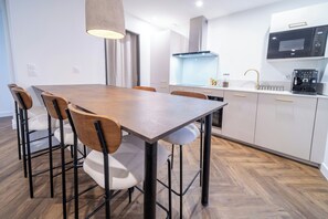 Eine moderne Küche mit Essbereich, ausgestattet mit einem Holztisch, Stühlen, einer Pendelleuchte und einer eingebauten Mikrowelle.