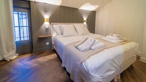Ein ordentlich bezogenes Bett mit Kissen und einem gefalteten Handtuch, ein Nachttisch und eine Wandleuchte.