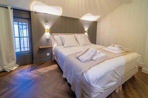 Ein ordentlich bezogenes Bett mit Kissen und einem gefalteten Handtuch, ein Nachttisch und eine Wandleuchte.