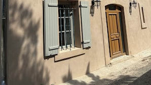 Ein Gebäude mit einer beige farbenen Fassade, einer Holztür und zwei Fenster mit Fensterläden.