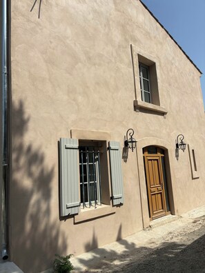 Ein Gebäude mit einer beige farbenen Fassade, einer Holztür und zwei Fenster mit Fensterläden.