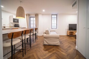 Ein modernes Wohnzimmer mit Holzboden, einer Couch, einem Esstisch mit Stühlen, einer TV-Konsole und einer Küchenzeile mit einer Mikrowelle.