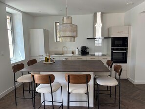 Una cocina moderna con una isla central, taburetes de bar, una cafetera y electrodomésticos integrados.
