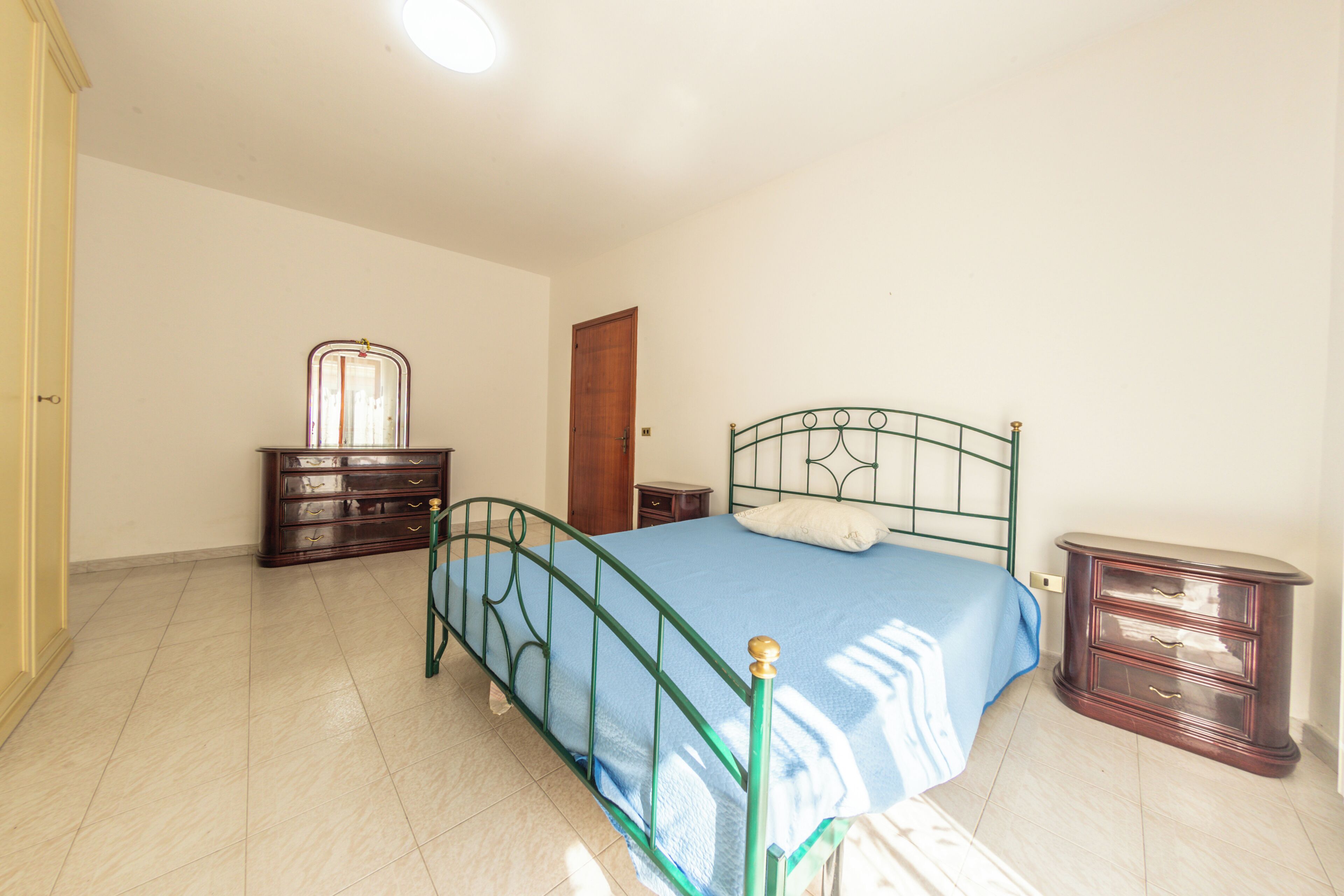 Un dormitorio con cama, cómoda, mesita de noche y una puerta.