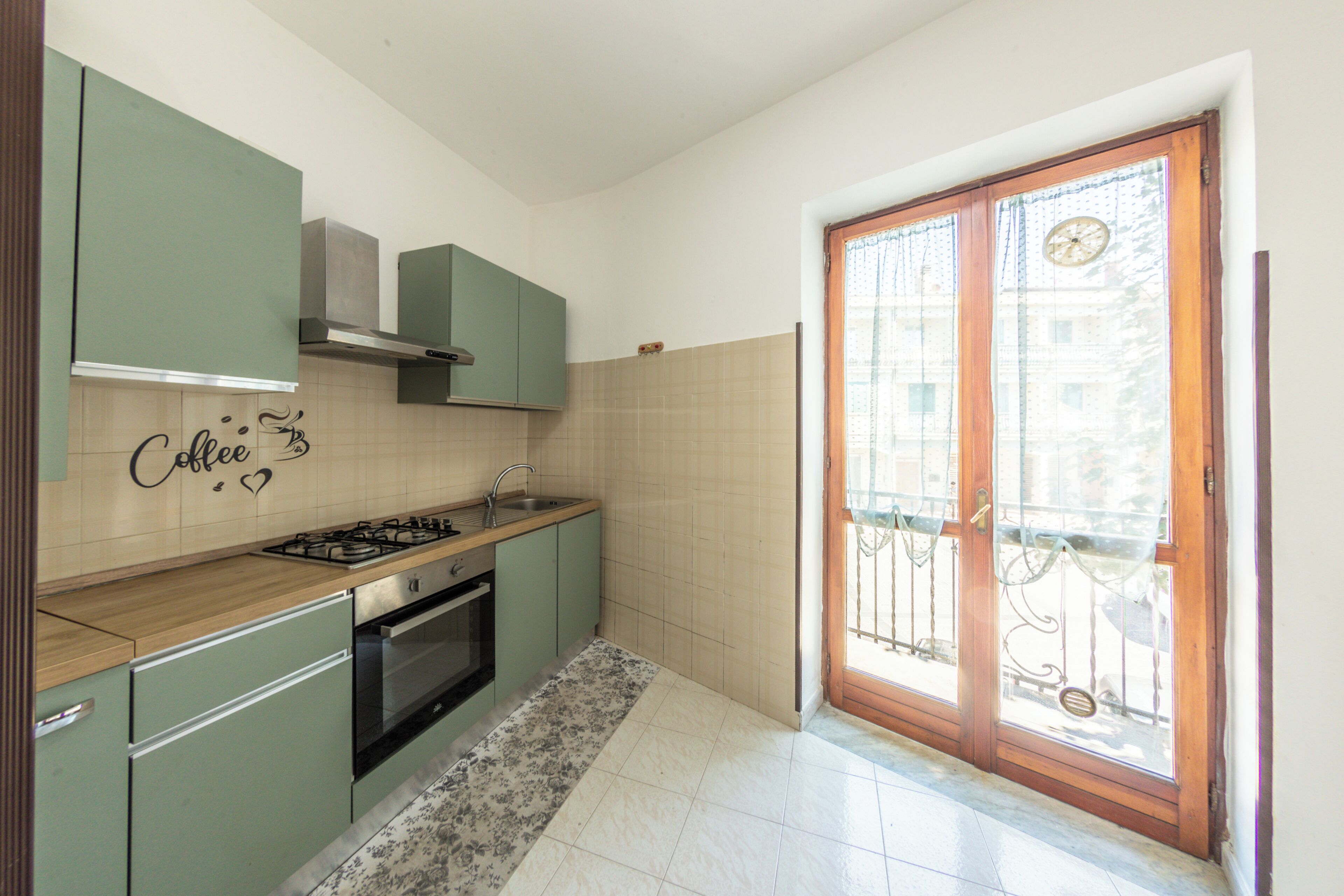 Una cocina con estufa a gas, horno y pileta. Hay una pared decorativa con un cartel alusivo al café.