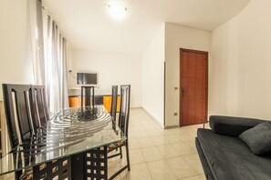 A dining area with a glass table and chairs, a television on a stand, a sofa, and a wooden door. - Andrè Casa Vacanza (Lioni)