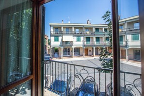 A view from a balcony with a metal railing, overlooking a street with buildings, a parked car, and a clear blue sky. - Andrè Casa Vacanza (Lioni)