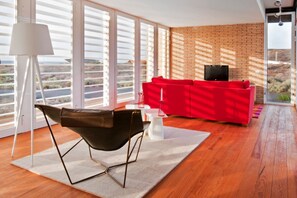 A modern living room with a red sofa, a black chair, and a TV on a brick wall. - Casas Bioclimáticas Iter El Alisio (Granadilla de Abona)