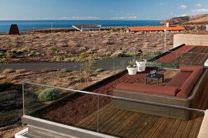 Une terrasse sur le toit avec une plateforme en bois, un espace salon avec des coussins et une vue sur l’océan.