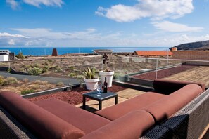 A rooftop terrace with a brown sofa, a small table with a glass and bottle, and potted plants. - Casas Bioclimáticas Iter El Alisio (Granadilla de Abona)
