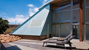 A modern building with a unique triangular facade, large windows, and a pool area with lounge chairs. - Casas Bioclimáticas Iter El Cangrejo (Granadilla de Abona)